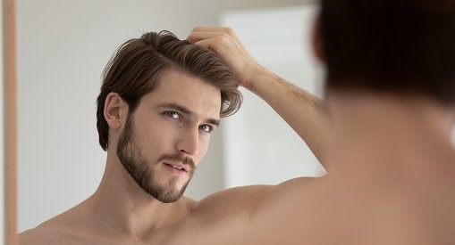 Young shirtless guy looks in mirror touch hair feels concerned due to receding, dry, dull hair. Hair loss common hair problem prevention, alopecia treatment ad, cosmetics products for male concept